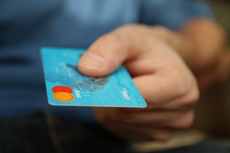 A close-up shot of a hand offering a blue debit card for payment.